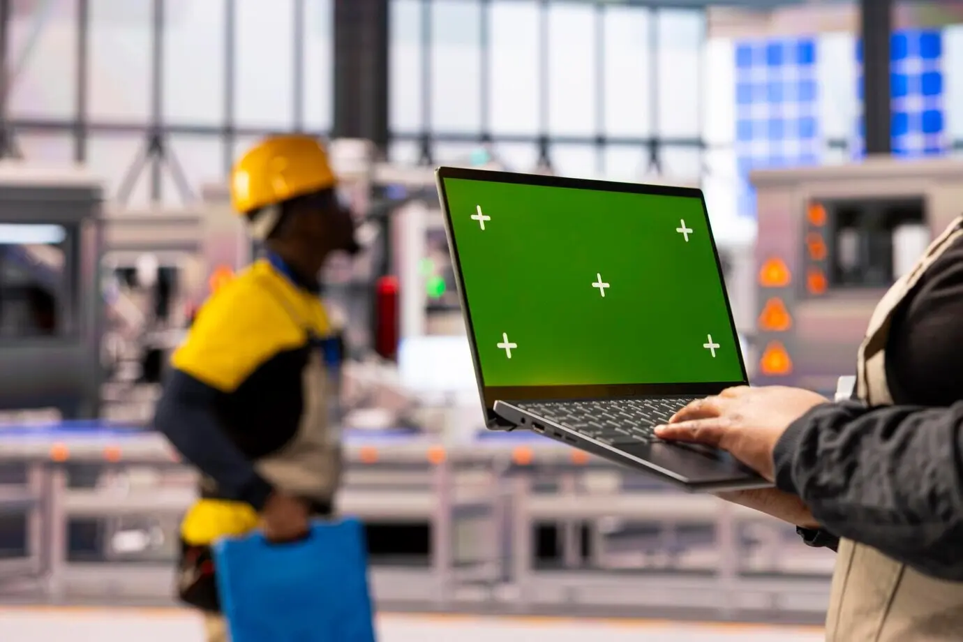 Эксперт по Индустрии 4.0 держит ноутбук с зелёным экраном на умной фабрике.